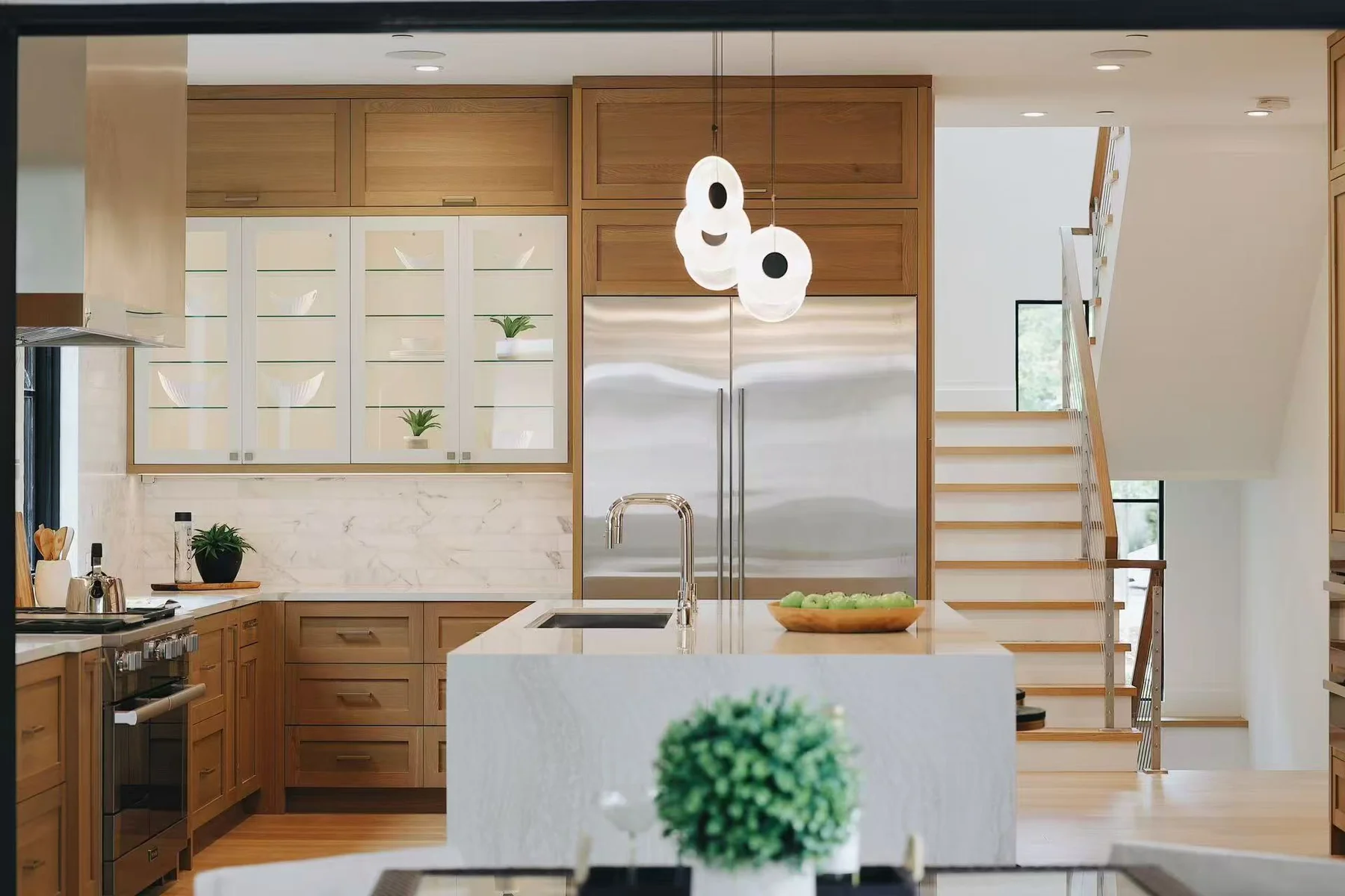 Frontal view of the kitchen island with pendant lights, refrigerator wall, and stair beyond