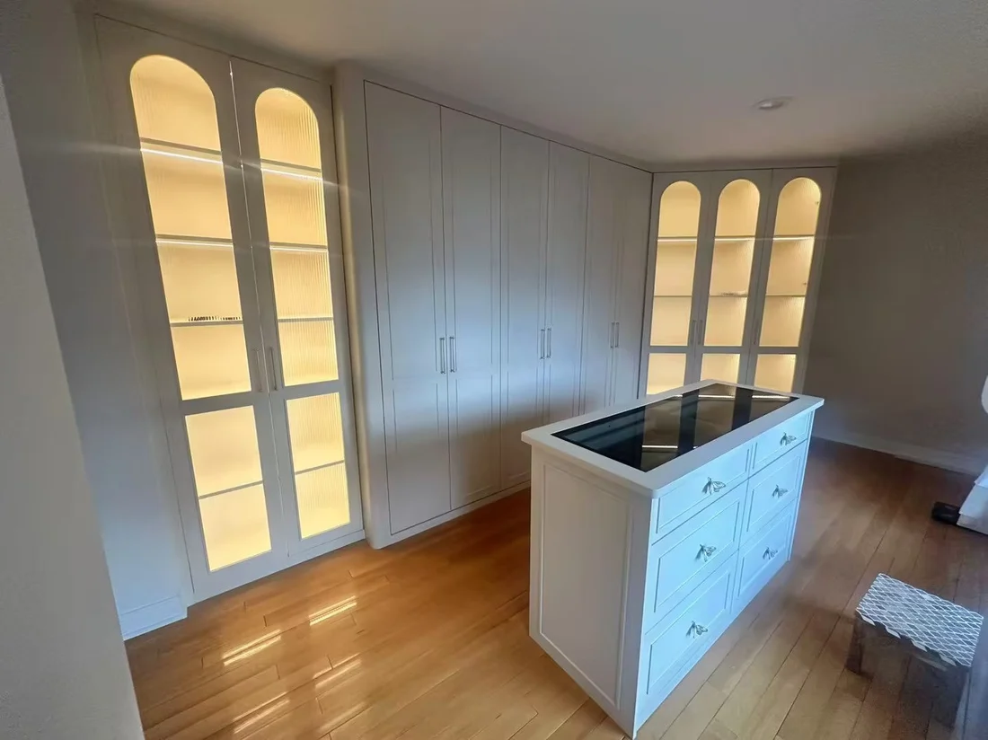 Completed New Jersey dressing room with cream lacquered cabinetry, lit arched fluted-glass display units and a stone-topped island