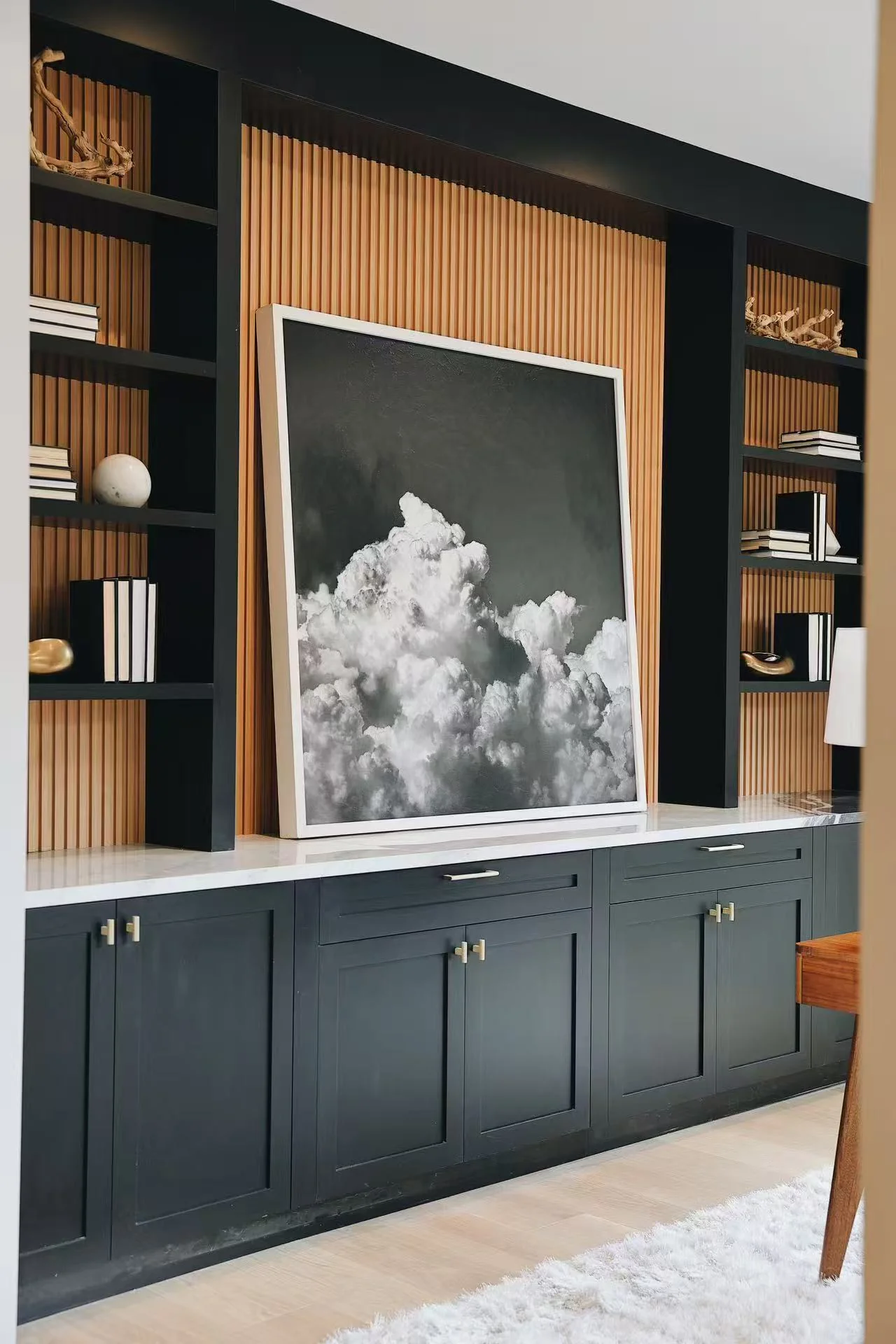 Custom built-in cabinet wall with black cabinetry, warm slatted timber back panel, art, and open shelving
