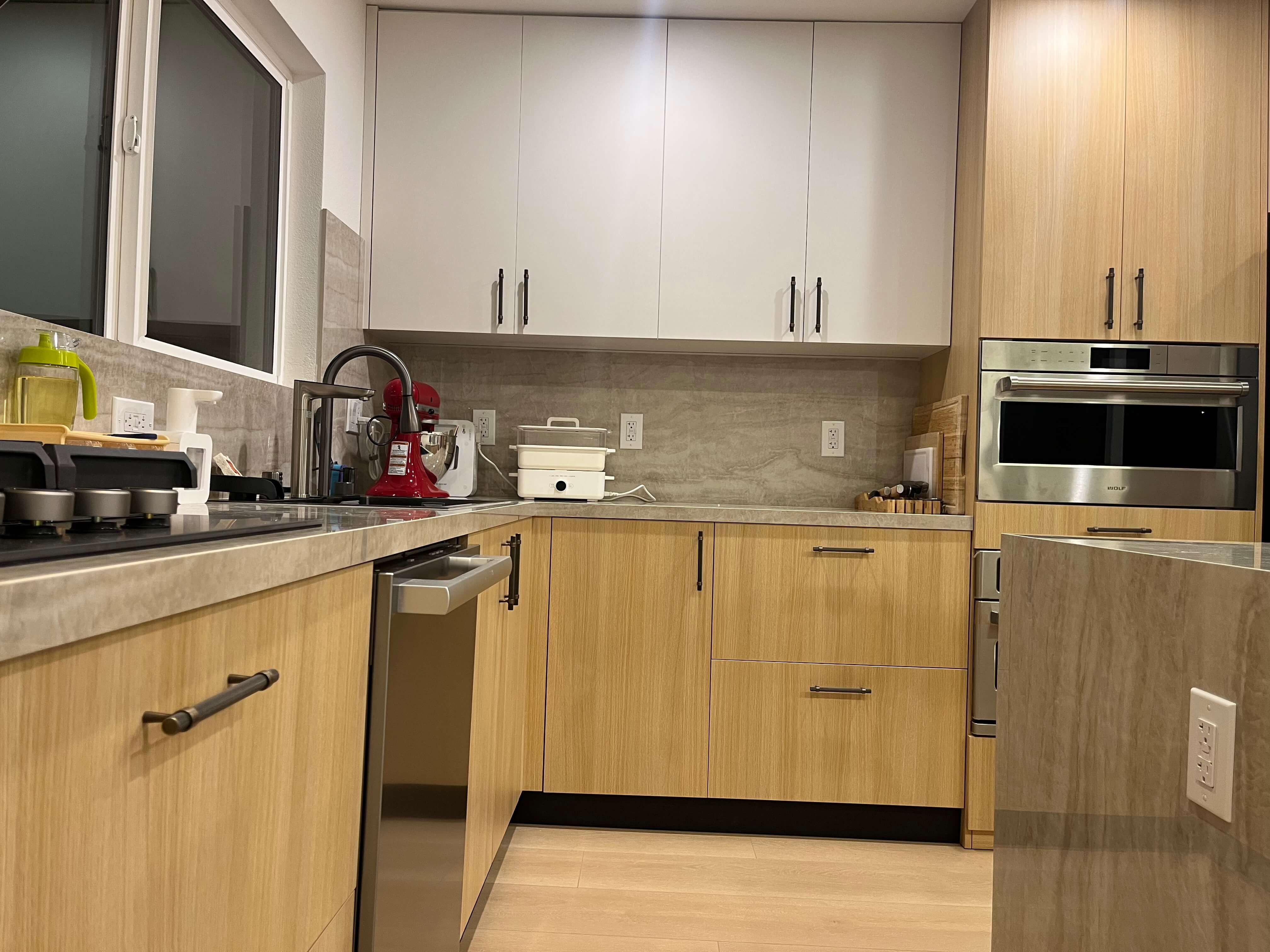 Wide view of the finished kitchen: stone island with seating, oak base run and white uppers
